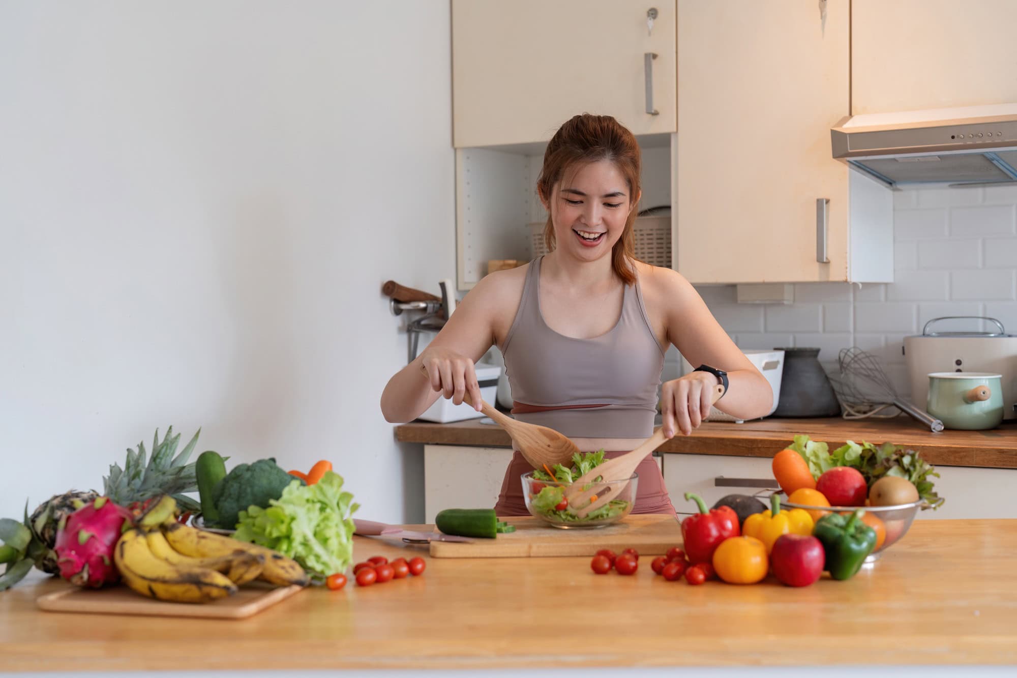 Young woman standing in the kitchen making a salad for health